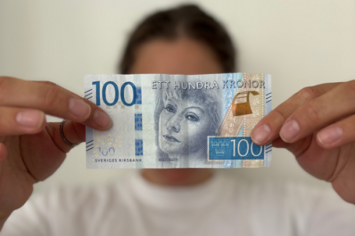 En kvinna i bakgrunden som håller fram en 100-lapp framför ansiktet